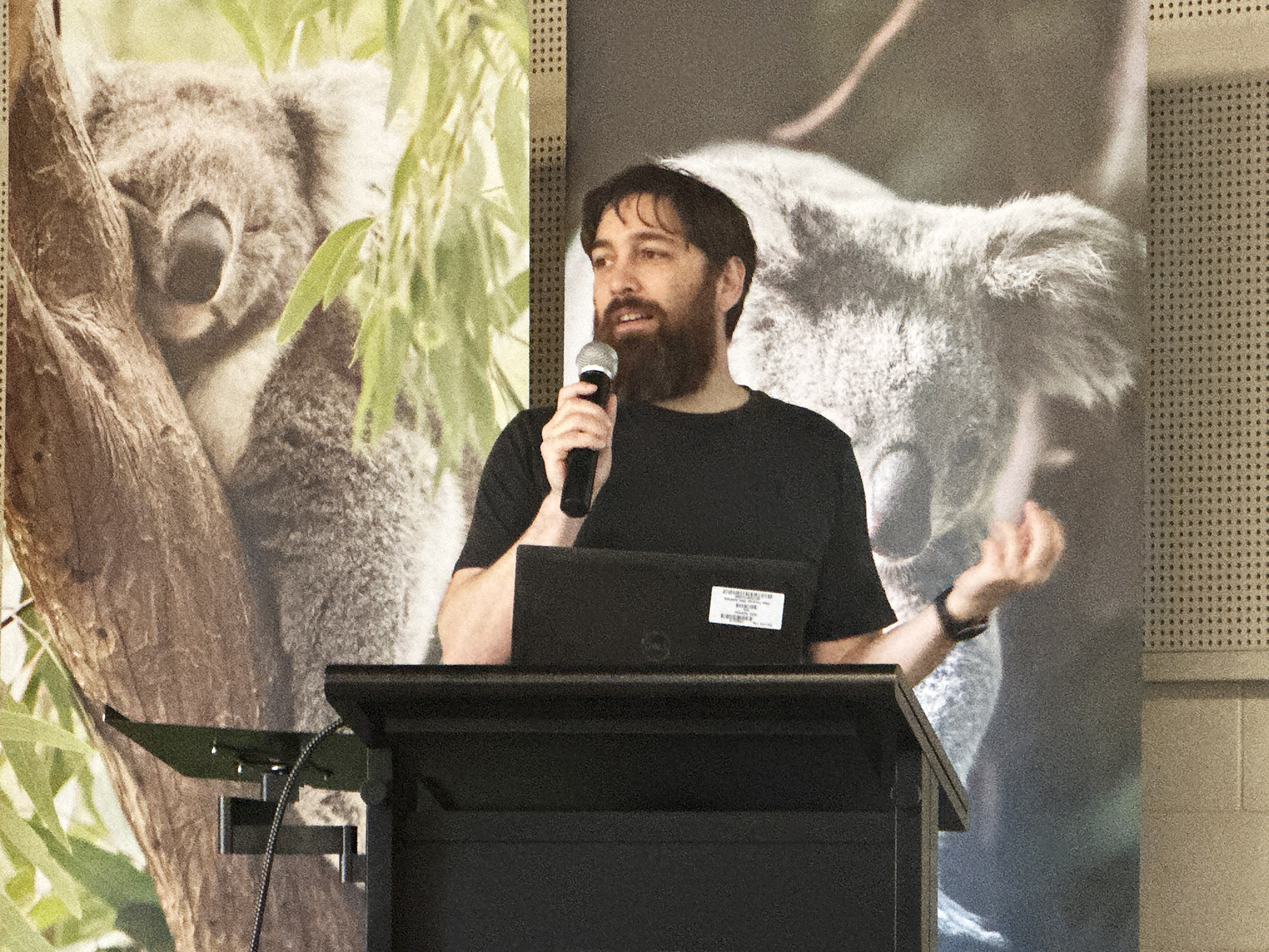 Andrew Hoskins speaking to an audience in front of large images of koalas